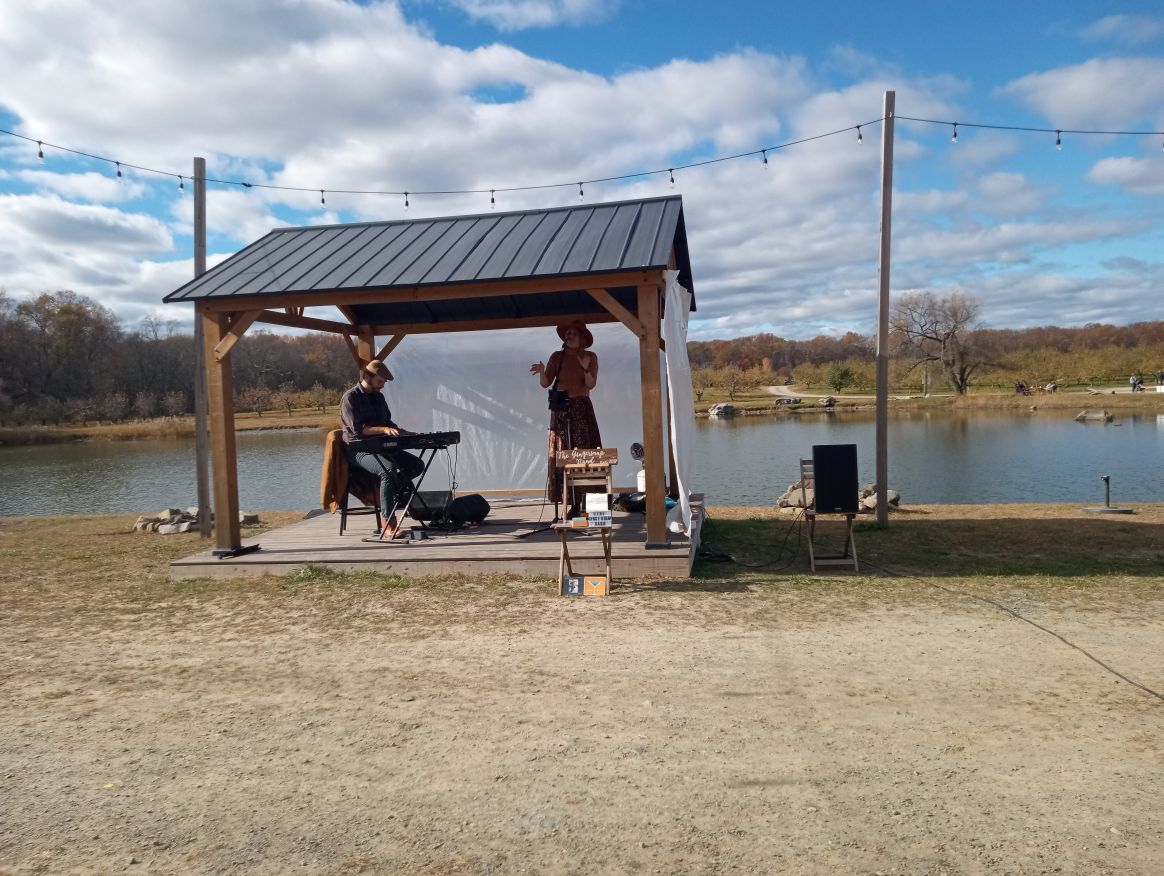 A man playing the piano and woman singing under a canopy with a lake in the background